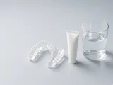 A clear whitening tray next to a white tube and a glass of water